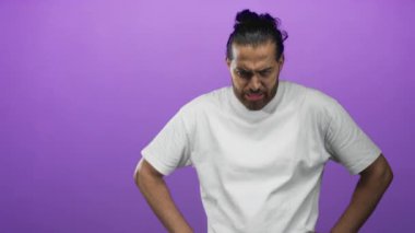 Mor stüdyoda elleri kalçasında kaşlarını çatan ve çenesini sıkan adam beyaz tişört giyiyor; öfke karşı koyma azmi.