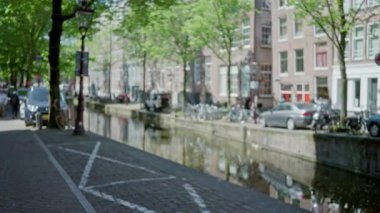 Amsterdam Kanalı 'nın bulanık manzarası bisikletlerle ve park halindeki arabalarla Hollanda' daki ağaçlık cadde boyunca, sakin bir şehir manzarası yaratarak, bokeh etkisi yaratıyor..