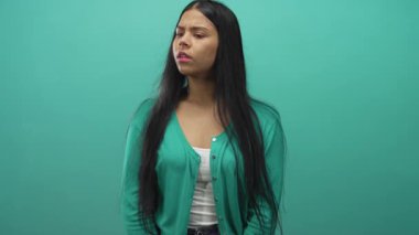 Avuç içleri kalkık ve ağzı açık Latin bir kadın stüdyoda sürpriz yaparken yeşil arka planda karmaşa yaratıyor..