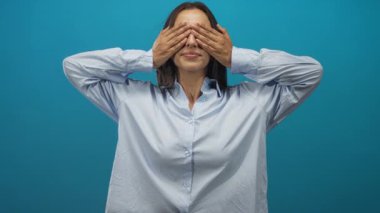 Ağzı kapalı gülümseyen genç İspanyol kadın ve parlak mavi stüdyoda avuç içi kaldırdı; sevinç kutlaması sıcaklığı.