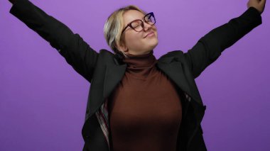 Kollarıyla muzaffer bir şekilde gülümseyen bir kadın canlı mor bir arka plan karşısında şık bir kıyafet ve gözlük takarken neşe ve kendine güveni somutlaştırıyor..