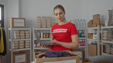 Kırmızı tişörtlü kadın dizüstü bilgisayarda bir binanın içinde giysi ve yemek kutusuyla yazıyor. Konsantrasyon..