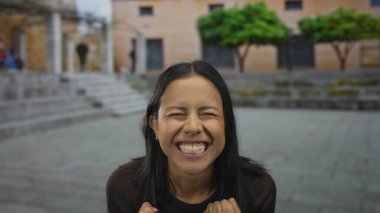 Kadın şehir sokak ortamında sevinçle kutlama yapıyor, arka planda ağaçlar ve binalarla dışarıda heyecan ve mutluluk ifade ediyor.