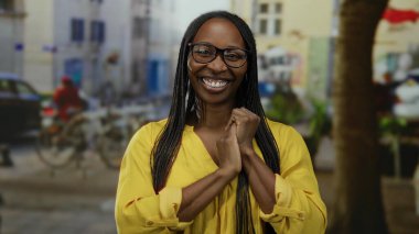 Şehir arka planında sarı gözlüklü bir kadın, canlı şehir hayatı ve açık havada mutluluk sergiliyor..