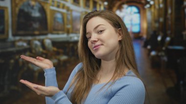 Mavi kazaklı kadın, müze binasının süslü galerisindeki yaldızlı tablolara doğru avuçlarını açıyor..