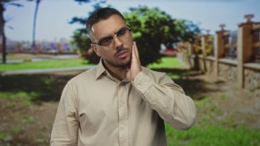 Yeşil ormanda diş ağrısı için el ele tutuşan gözlüklü ve açık renk gömlekli bir adam..