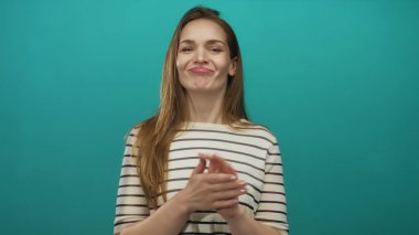 Genç Kafkas kadın geniş bir gülümseme içinde bir deniz mavisi stüdyosunda nazik bir ritimle el çırpıyor; sevinç destek alkışlarını kutluyor.