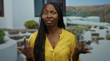 Şehir merkezinde sarı gömlekli bir kadın taş basamaklar ve bitkilerin yanında şaşırmış bir ifade sergiliyor..