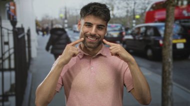 Adam, kalabalık şehir caddesinde arabaları ve yayaları ile geniş bir gülümseme ile parmak yanağa dolaşırken; mutluluk.