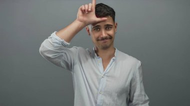 Genç İspanyol bir adam, elini yalıtılmış gri bir arkaplan üzerinde tutar ve ince bir ifadeyle özgüvenini iletir..