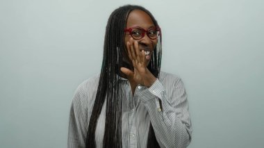 Uzun saçlı ve gözlüklü gülümseyen bir kadın saf beyaz bir duvarın arkasında neşeli bir hareketle izole edilmiş.