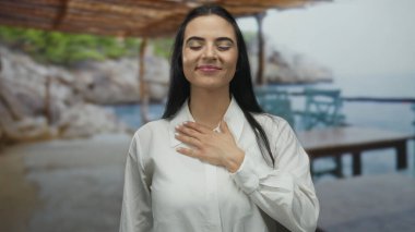 Deniz kenarındaki bulanık arka planda gülümseyen bir kadın güneşli bir günde sakin ve barışçıl bir tavır sergiliyor..