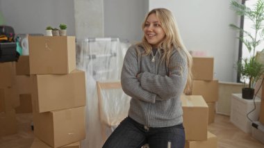 Yeni bir dairede gülümseyen bir kadın. Etrafı çiçeklerle dolu, rahat bir oturma odasında kutuları taşıyor. Günlük kıyafetler giyiyor, rahat bir ortamda yeni bir başlangıç yapıyor..