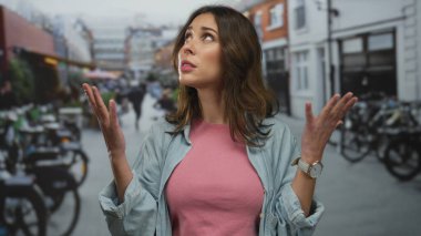 Çevresi bisiklet ve şehir manzarasıyla çevrili, hareketli bir şehir sokağında hareketli genç İspanyol kadın, açık havada günlük giysiler ve kol saati giyiyor..