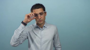 Genç İspanyol adam dikkatle ayarlar ve mavi bir stüdyo ortamında şeffaf gözlük çerçeveleri çıkartır;.