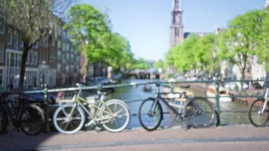 Amsterdam 'da bir köprüde bisikletler. Arka planda bulanık kanallar ve yeşil ağaçlar güneşli bir günde bokeh etkisi yaratıyor..