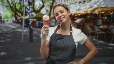Sokak terasında elinde dondurma külahı tutan kadın kot önlüklü ve eldivenli; keyif yaz ziyafeti.