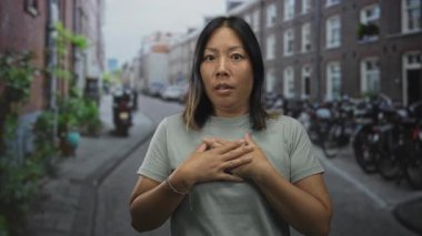 Bisikletler ve tuğla evler ile kaplı dar kaldırımlı bir sokakta el ele tutuşan, geniş gözlü ve çatık kaşlı bir kadın..