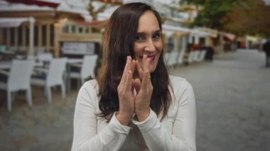 Şehir caddesindeki açık hava restoranının terasında gülümseyen bir kadın doğal ışıkta neşeli bir ifadeyle el çırpıyor..