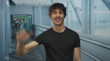 El sallarken ve havaalanı terminalinde parmaklarını aşağı doğru gösterirken ağzı açık gülümseyen bir adam..