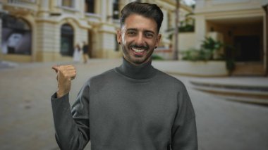 Genç İspanyol asıllı bir adam şehir meydanındaki kaldırım taşı caddesindeki süslü binayı işaret ediyor. İyimserlik..