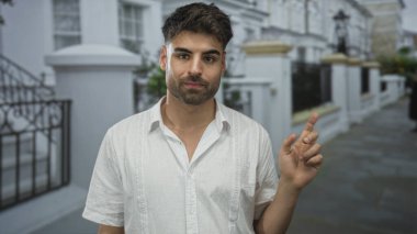 Genç İspanyol adam, güneşli şehir caddesinde beyaz bina cephesiyle el sallıyor. Reddedildi..