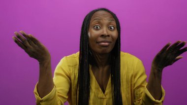 Renkli pembe arka plana karşı anlamlı yüzlü, sarı tişörtlü bir kadın hareketleri izole edilmiş bir stüdyoda saç örgüleriyle ruh halini ve duygularını gösteriyor..