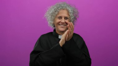 Ruhban sınıfından gri saçlı bir kadın canlı pembe arka plana el çırpıyor neşeli ve ruhani duyguları vurguluyor..