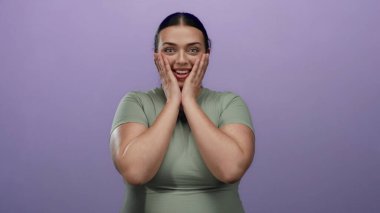 Canlı mor bir duvara karşı neşeli bir şekilde poz veren kadın, kendine güven ve neşe saçan, açık yeşil bluzlu, izole edilmiş stüdyo ortamlı, büyük boy bir moda tarzı sergiliyor..