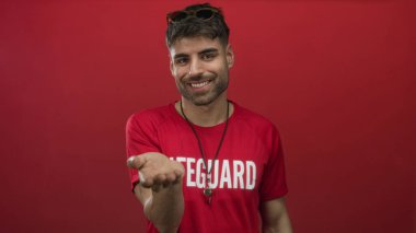 Cankurtaran, parlak kırmızı stüdyo ortamında boynunda asılı gümüş düdük ile elini teklif; güven.