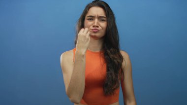 Gergin ifadeli İspanyol kadın, mavi stüdyo ortamında parmaklarını çimdiklediğini ve kaşlarını çattığını gösteriyor. Hayal kırıklığı..