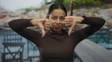 Açık hava restoranının terasında, arka planda gündüz aydınlatma koşullarında açık hava oturma ve bulanık sokakları tasvip etmeyen bir kadın var..