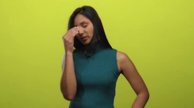 Latin bir kadın, kolsuz, yeşil bir üst jestle parlak sarı bir arkaplanda izole edilmiş bir şekilde samimi bir ilişki ve duygu anı yakalıyor..