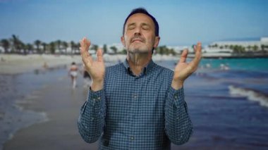 Huzurlu bir plajda duran, gözleri kapalı, deniz ve güneşin sakinliğinin tadını çıkaran, deniz kenarındaki bir dinlenme ve huzur içinde meditasyon yapan bir adam..