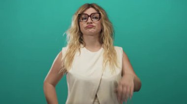 Sarışın, gözlüklü, eli çenesinde, eli kalçasında, göktaşı arkaplanlı, düşünceli genç bir kadın..