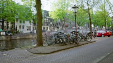 Gündüz vakti arka planda bulanık binalar ve ağaçlarla dolu Amsterdam Kanalı boyunca park edilmiş motorlar..