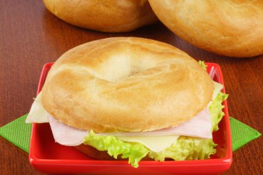 Sade simit, jambon, peynir ve marul, ahşap bir arka planda kırmızı bir tabakta..