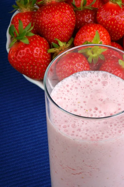 草莓奶昔特写和一些新鲜的草莓在前景在深蓝色桌布 — 图库照片