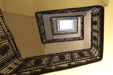 Parlak bir ışık kaynağına doğru yükselen zarif, işlenmiş demir bir merdivenin alçak açılı görüntüsü