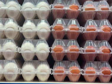 Beyaz ve kahverengi tavuk yumurtaları şeffaf plastik kaplarda, süpermarketin rafına istiflenmiş, satın alınmaya hazır.