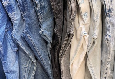 Farklı renklerde kot pantolonlar, çamaşır makineleri ve stiller asılıyor ve bu popüler giysi ürününün görsel olarak çekici bir görüntüsünü yaratıyor.