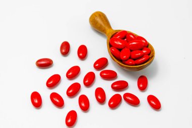 Tahta kaşıkta kırmızı haplar, beyaz arka planda izole edilmiş..