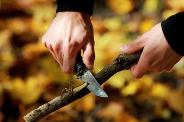 Bir adam bir dalı bıçakla keskinleştirir.