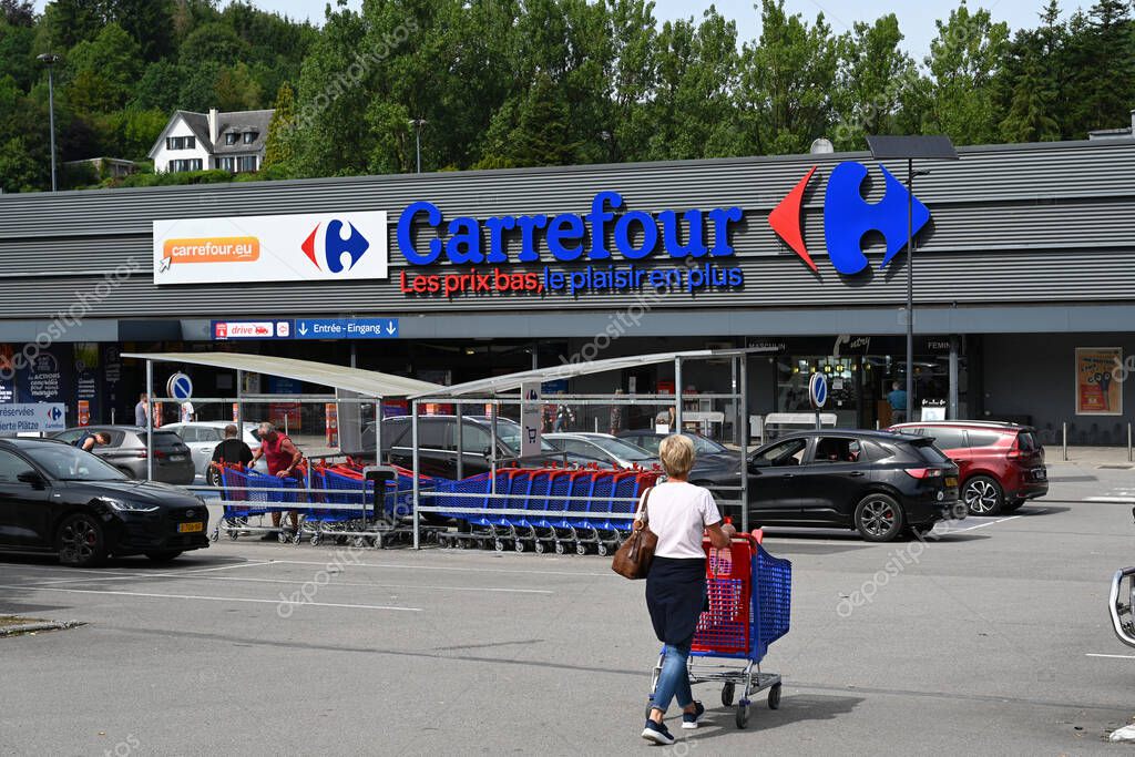 MALMEDY, BELGIUM - AUGUST 2023: Woman with shopping cart goes shopping in a Carrefour hypermarket. Text slogan under the trade name is: low prices, more fun