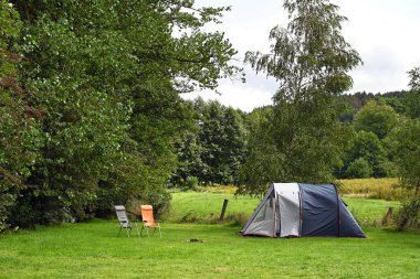 Belçika Ardennes 'deki kamp alanının çimlerinde polyester tünel çadırı ve kamp sandalyeleri.