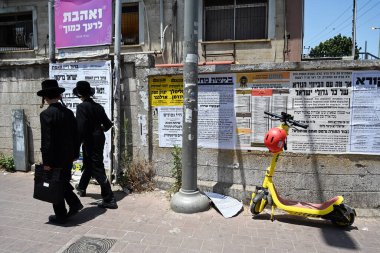 BNEI BRAK, ISRAEL - Mayıs 2023: İbranice pankartlarla kaplı iki Hasidik Yeshiva öğrencisi çocuk duvarın önünden geçiyor.