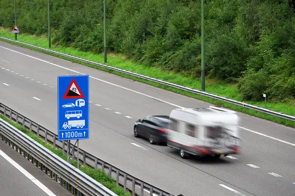 Car with travel trailer, passes a traffic information sign on highway E42, the route through the Belgian Ardennes near Malmedy