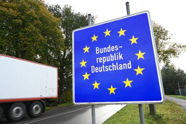 Mavi Yol İşareti: 'Bundesrepublik Deutschland', Almanya Federal Cumhuriyeti. Hollanda sınırı yakınındaki imza panosundan Almanca yazılmış kamyonet geçiyor..