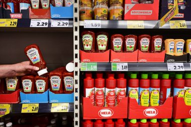 GERMANY - Haziran 2024: Alışverişçi, Kaufland süpermarketinde satılmak üzere çeşitli soslar ve ketçaplar içeren raflardan Heinz marka domates ketçapı seçti