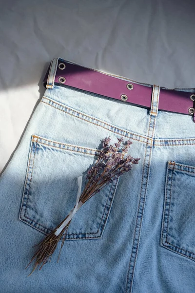 stock image Blue jeans with lavender bouquet on white fabric background.